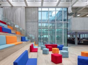 A bright, modern lecture space with large windows and colorful blue, yellow, and red tiered seating.