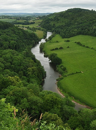 This is a picture of the River Wye it shows the river running through a Valley with flat Fields either side and with its loops wooded slopes